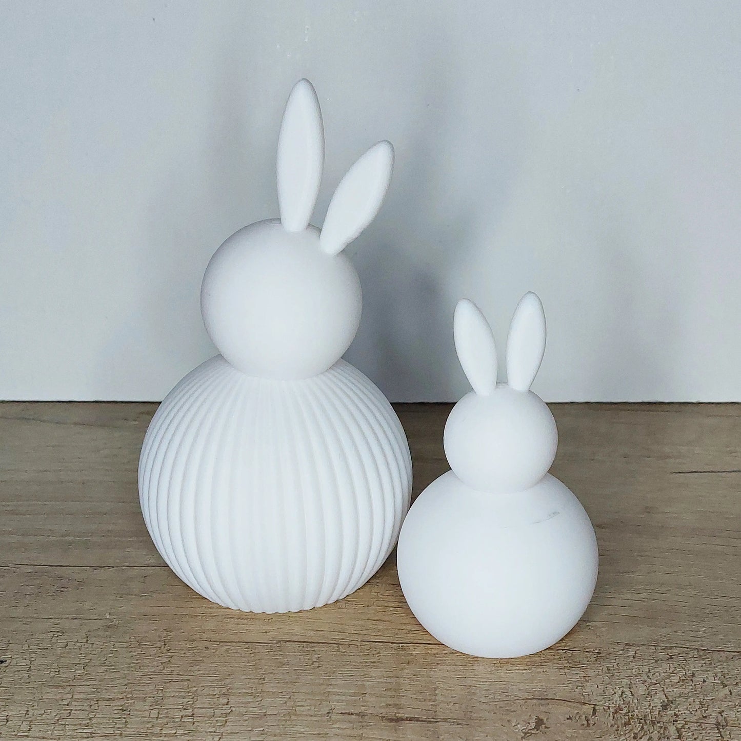 Two white 3D-printed bunny figures, ribbed and smooth, on a wooden surface from megahobby3dcreations.